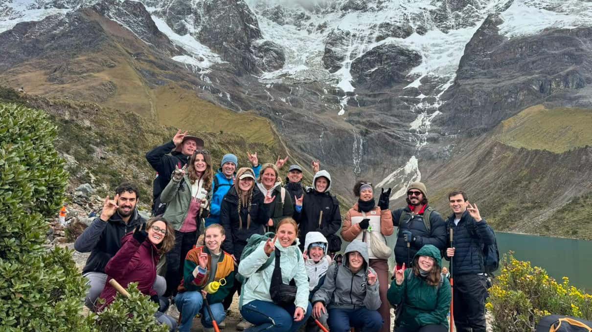 A smiling hiking group posing on the rocks in front of a glacier and snowy peaks