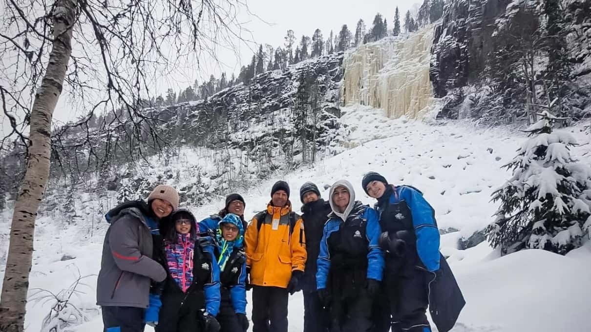 A group of hikers in winter clothes posing in the snow in front of Korouoma's frozen waterfalls