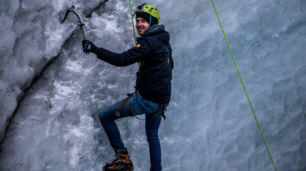 A climber on a grey ice wall of Sólheimajökull with a green rope running up beside him
