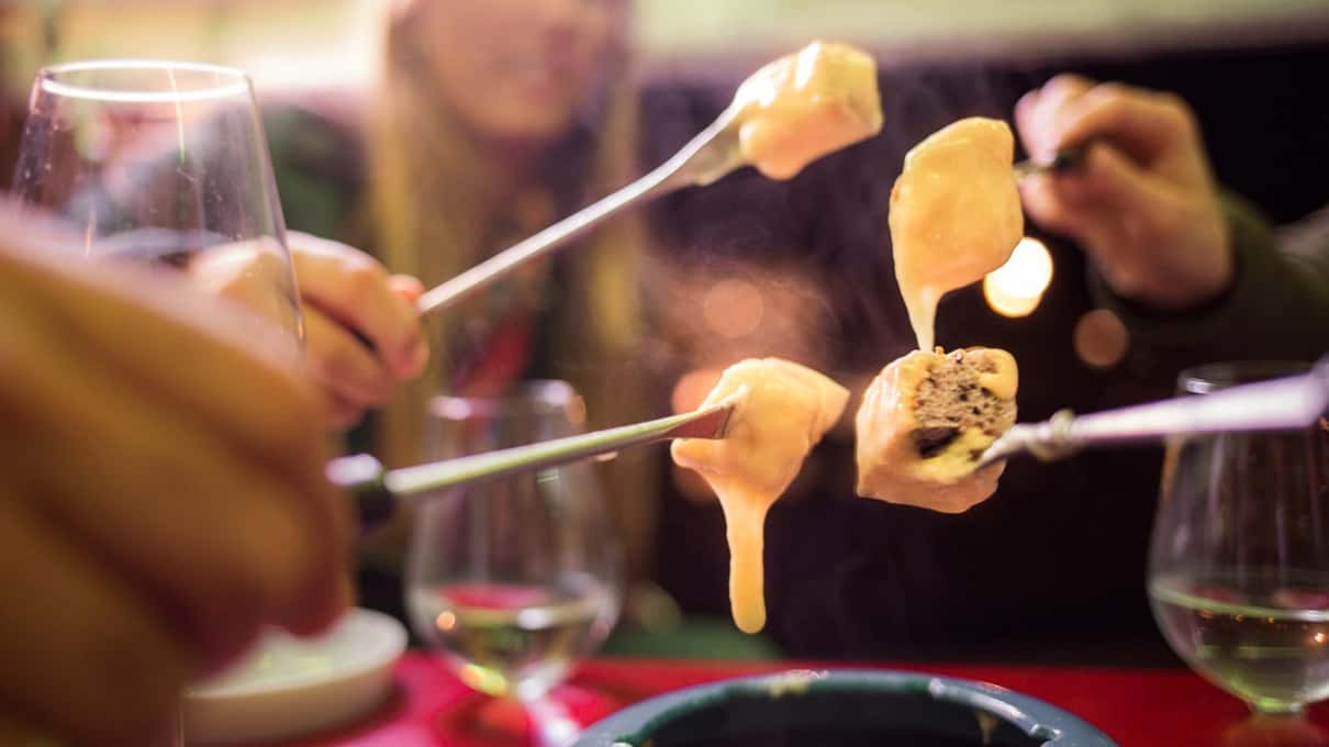 Two forks lifting cubes of bread out of a pot of fondue with strings of melted cheese