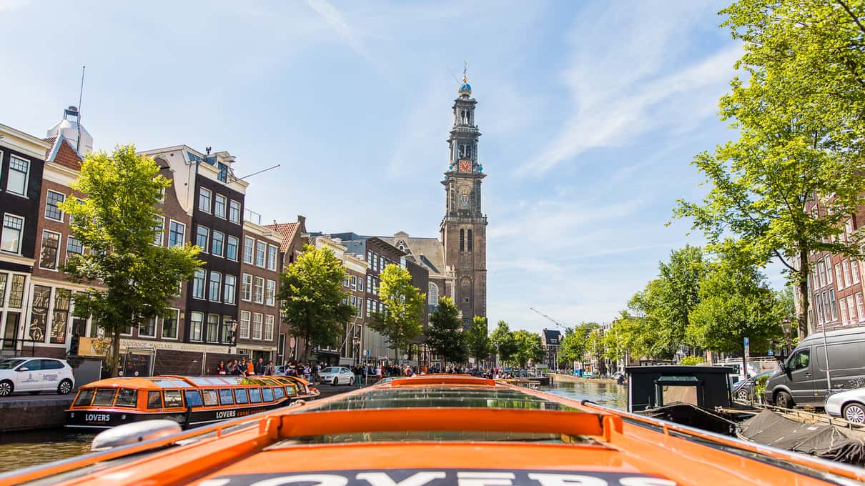 Oranje rondvaartboten afgemeerd aan een Amsterdamse gracht met de toren van de Westerkerk op de achtergrond