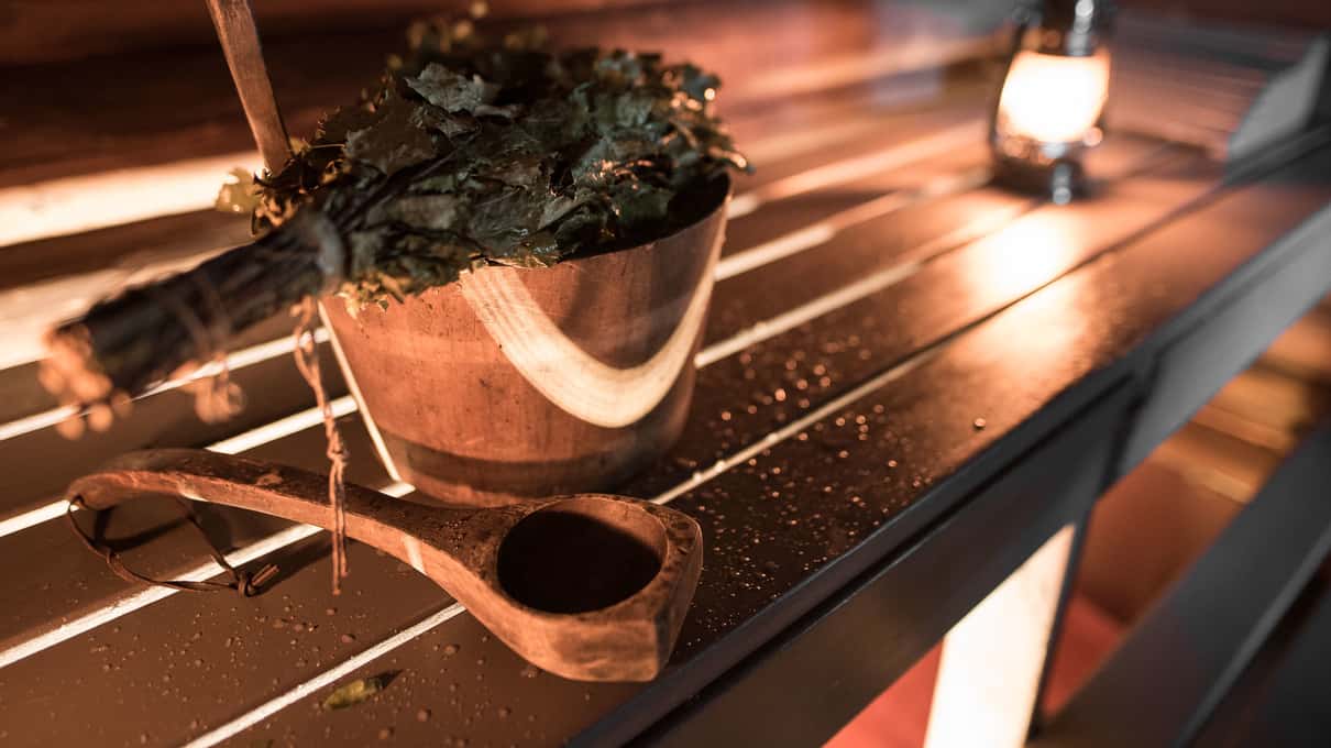 A wooden sauna bucket and ladle on a bench in warm sauna light