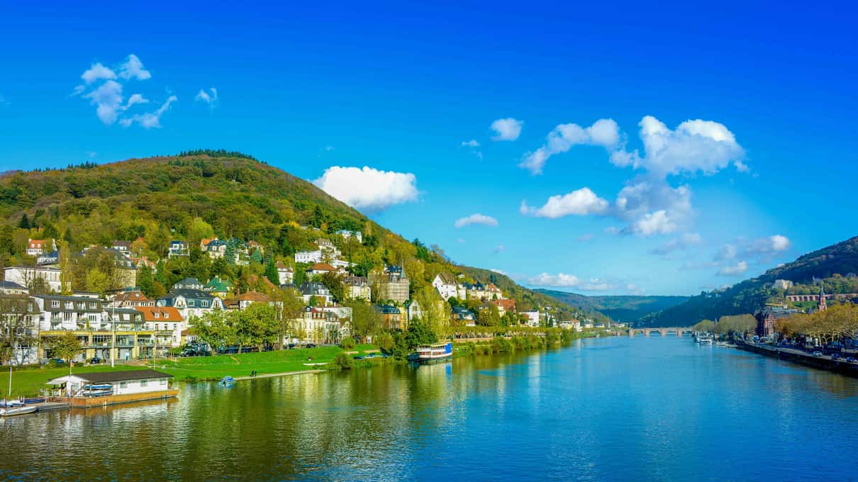 A Rhine village of white houses below steep vineyard slopes, with a passenger boat moored at the riverbank