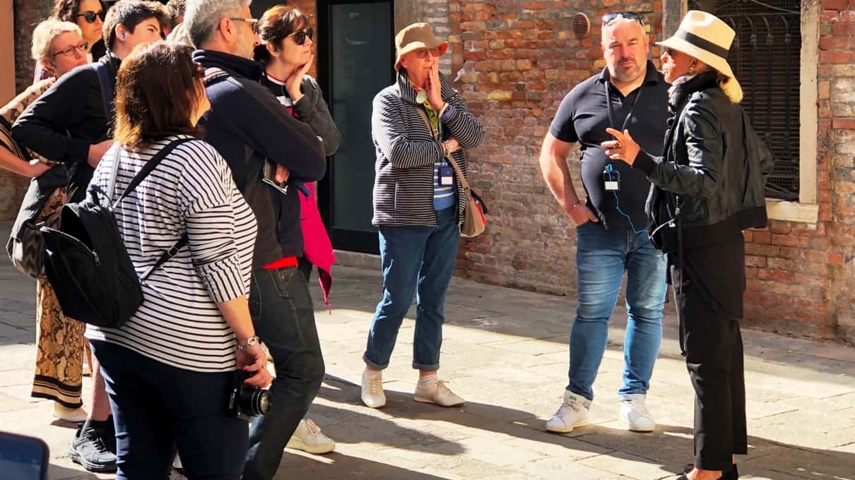 Guía con sombrero de paja explicando a un grupo de viajeros en una calle de Venecia con fachadas de ladrillo