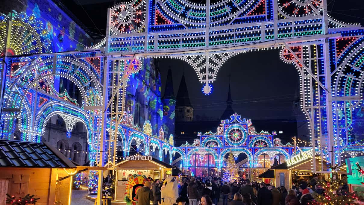 Arches of white and blue lights over the Landesmuseum courtyard at blue hour, with market huts below