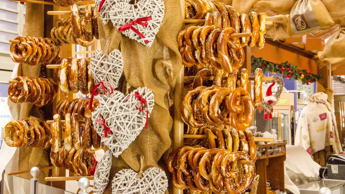 Rows of pretzels hanging at a Christmas market stall beside straw hearts and red ribbons