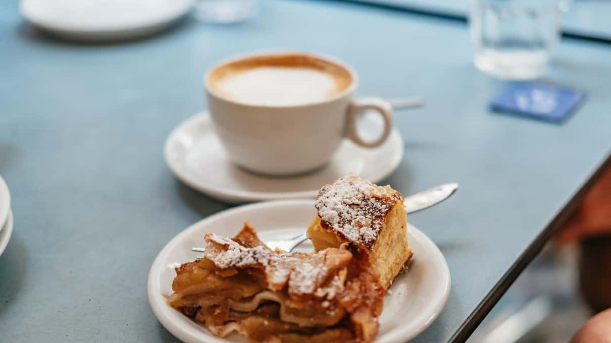 A cup of Viennese coffee and a slice of apple strudel on a marble coffee house table