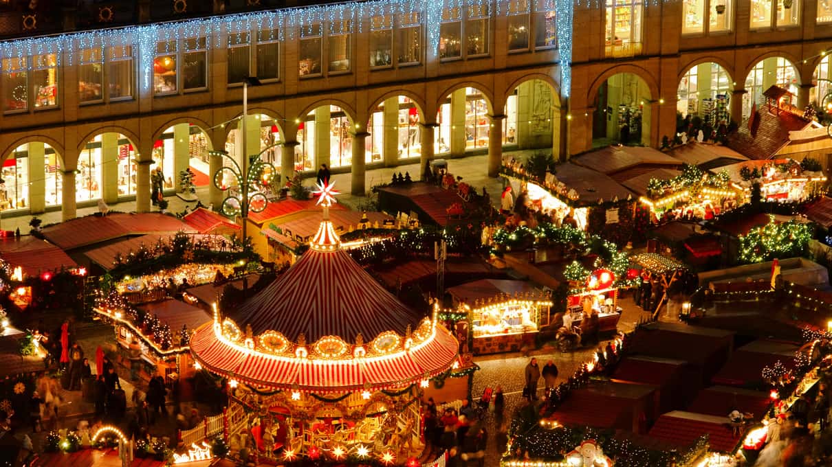 A lit carousel in front of the arcades of the Dresden Christmas market at night