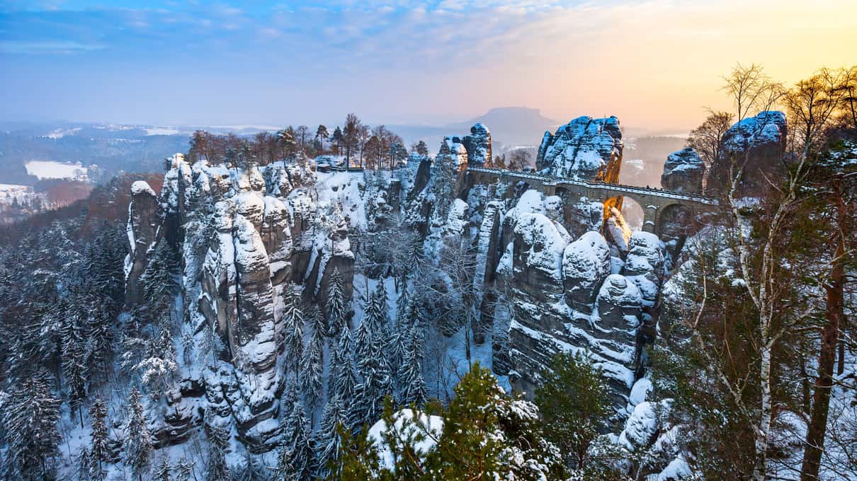 The sandstone rock towers of the Bastei in Saxon Switzerland dusted with snow above a wooded valley