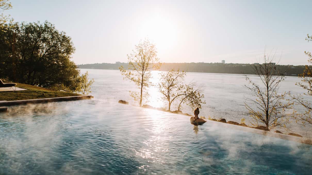 A bather in a steaming outdoor pool at Strøm Nordic Spa facing the St Lawrence in low sun