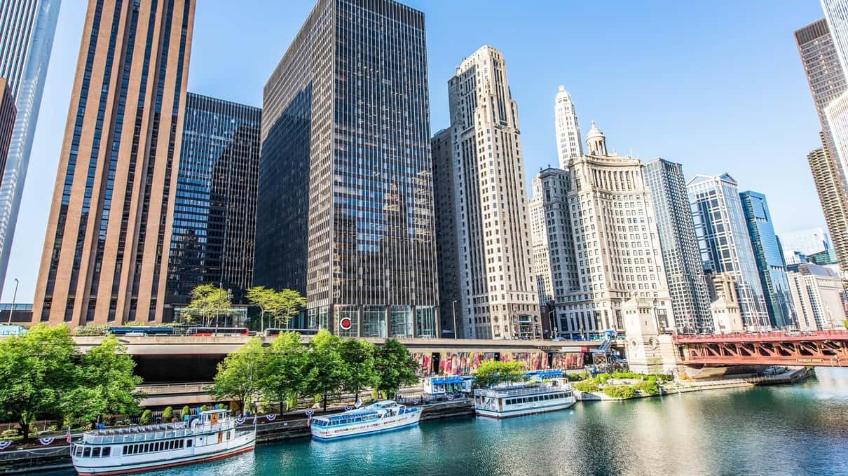 Dunkle moderne Hochhäuser und ältere Hochbauten säumen beide Ufer des Chicago River unter klarem blauem Himmel