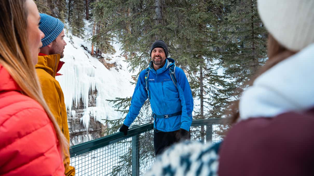 Smiling guide in a blue jacket and beanie with hikers and frozen falls behind him in Johnston Canyon