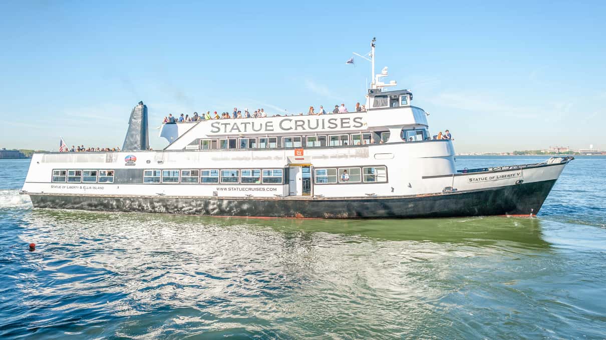 White Statue City Cruises ferry with passengers on its top deck crossing the harbor