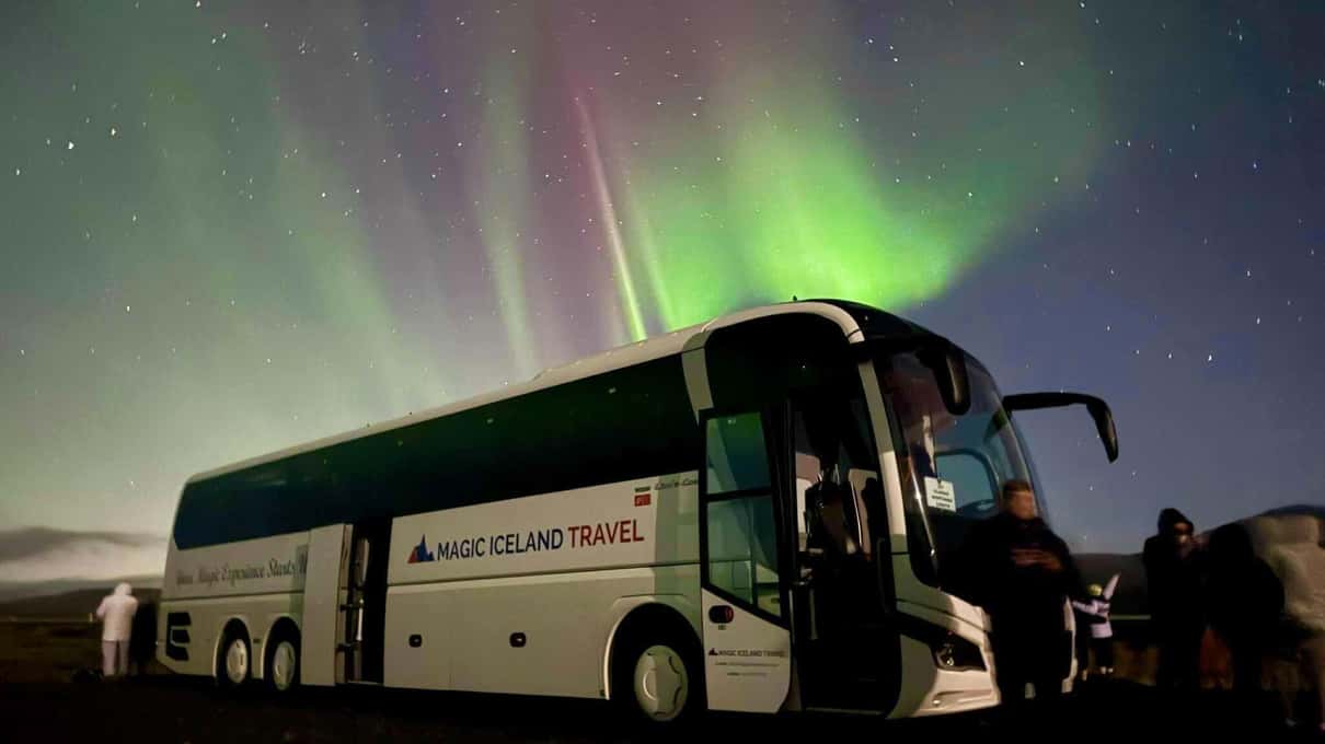 Moderner Reisebus der Nordlichter-Tour mit geöffneter Tür unter rosa und grünem Polarlicht