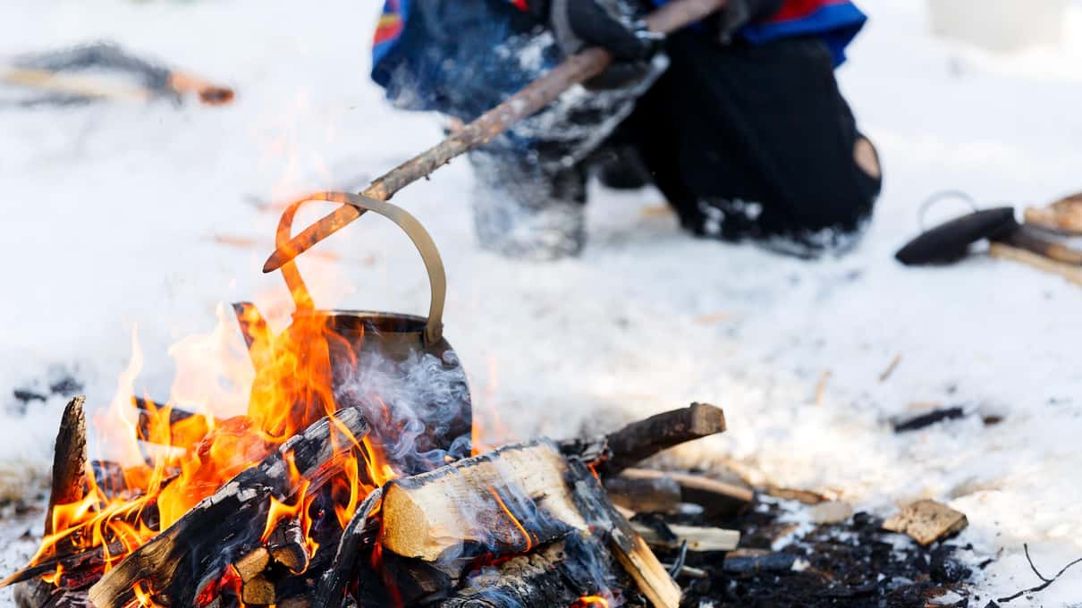 A sooty kettle hanging over a campfire on the snow of a frozen lake