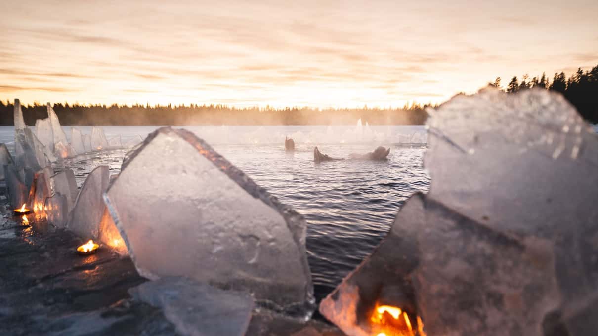 Blocks of lake ice lit by candles at dusk beside the floating hole on a frozen Lapland lake