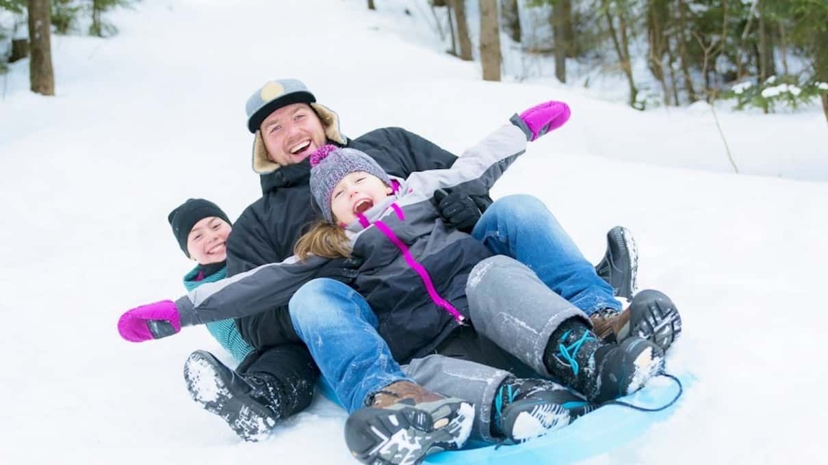 A family laughing as they slide down a snowy slope together on a tube
