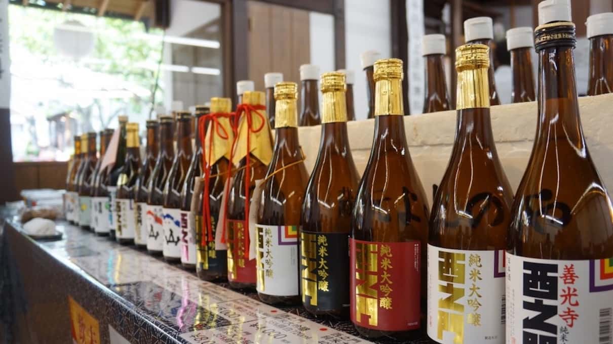 Rows of sake bottles with colorful labels lined up on a brewery shelf during the Zenko-ji and sake day