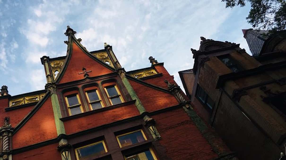 Low-angle view of a red-brick Victorian facade with ornate stepped gables against a clear blue sky