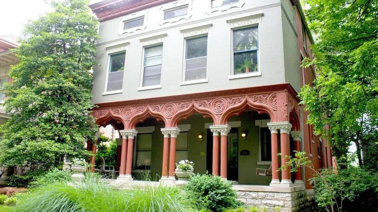 A two-storey cream house with a row of coral-red Moorish arches running across its front porch