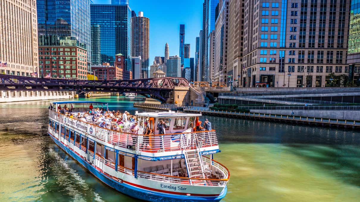 White and red sightseeing boat full of passengers cruising the Chicago River between glass towers