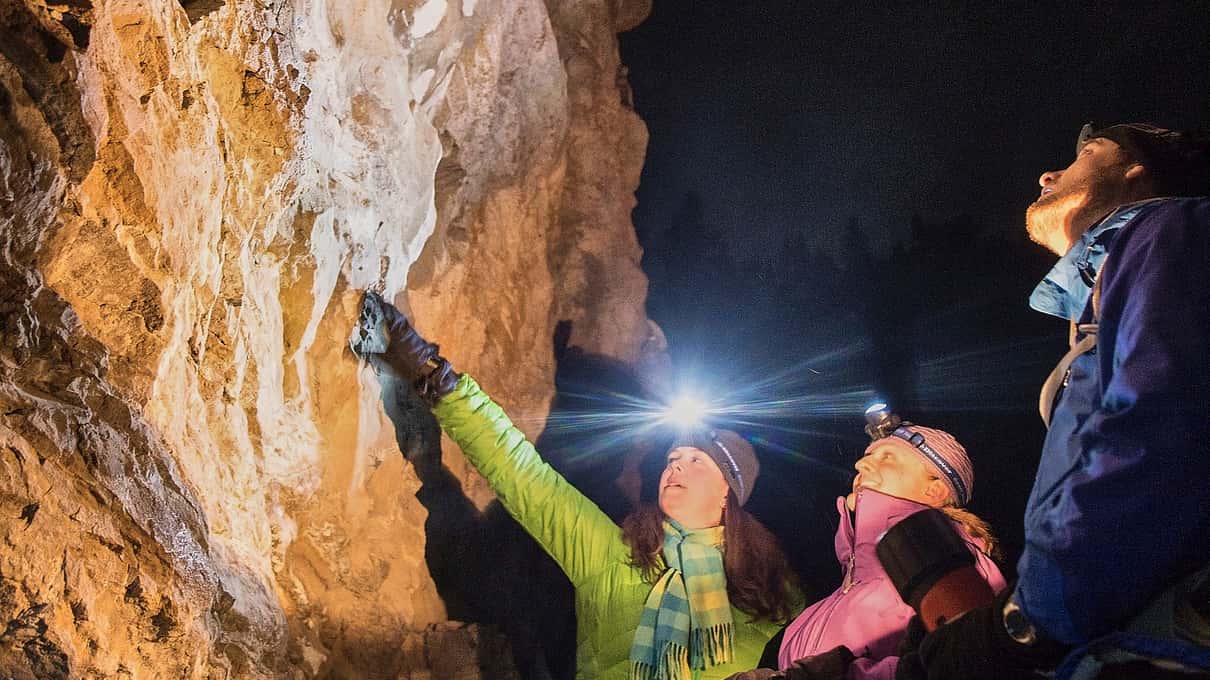Hikers wearing headlamps pointing at a wall of ice and rock inside Johnston Canyon at night