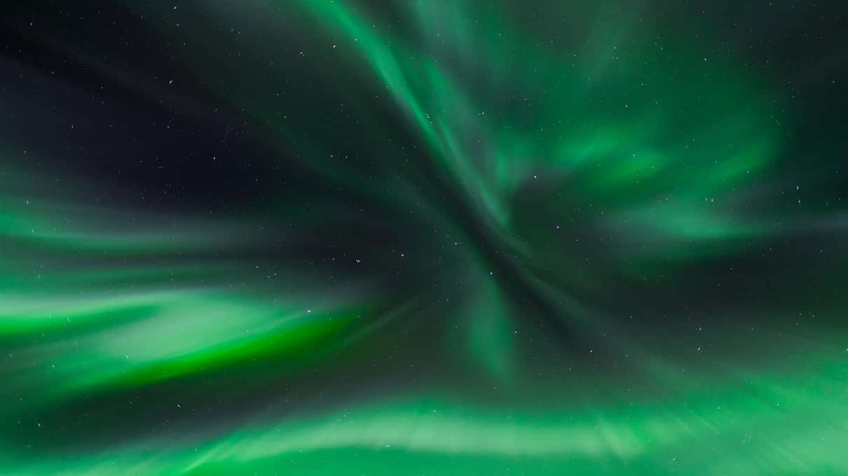Green aurora rays converging high overhead in a starry winter sky