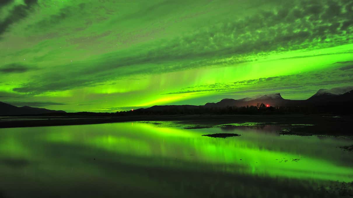 Green aurora reflected in still dark water below a mountain ridge near Abisko