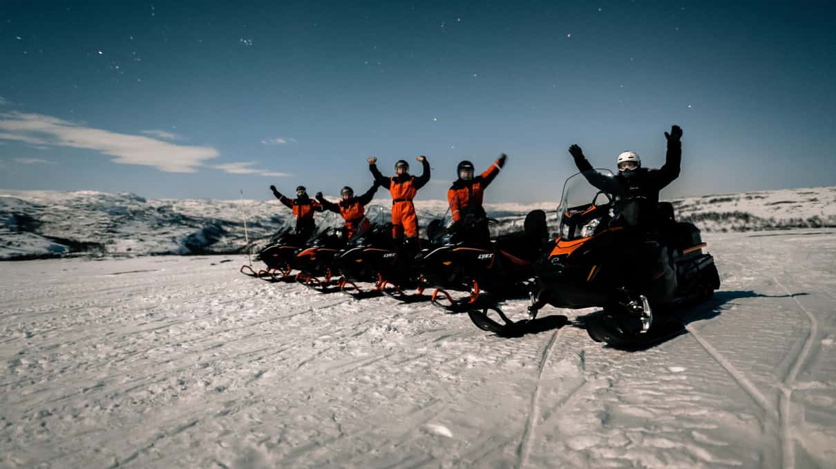 A line of riders cheering on their snowmobiles on the snowy plateau above Alta