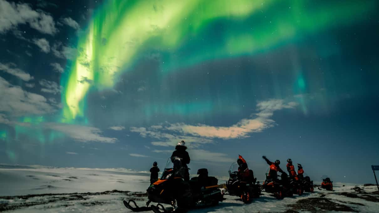 A green aurora arc over the dark Finnmarksvidda plateau above a group of snowmobiles