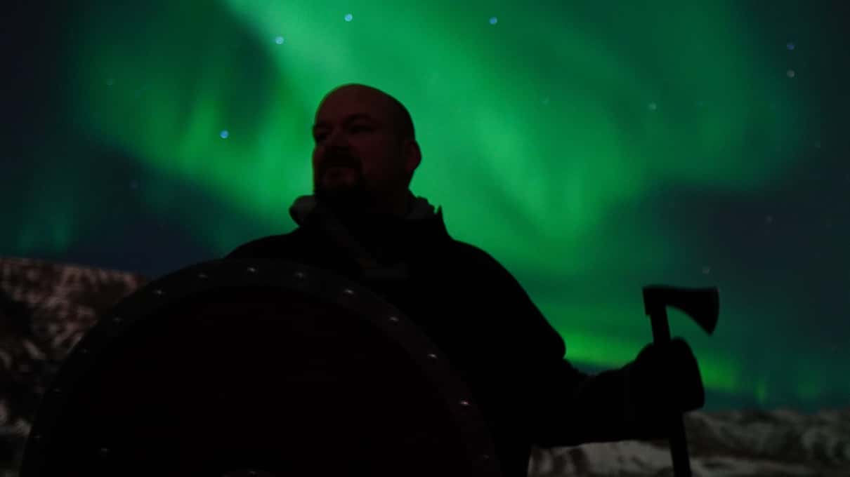 The silhouette of a guest holding a replica Viking axe against a bright green aurora