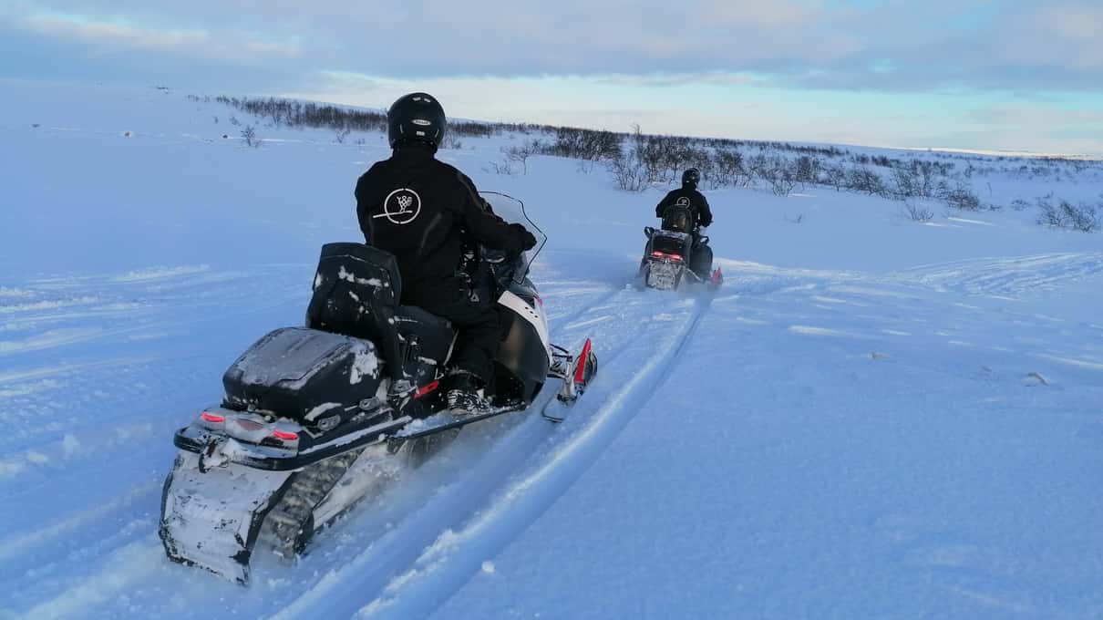 A lone snowmobile parked on a wide white plain of Finnmarksvidda under a big open sky