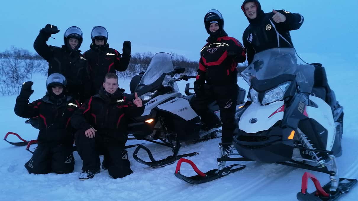 A small group of riders posing beside their snowmobiles on the open Finnmarksvidda plateau