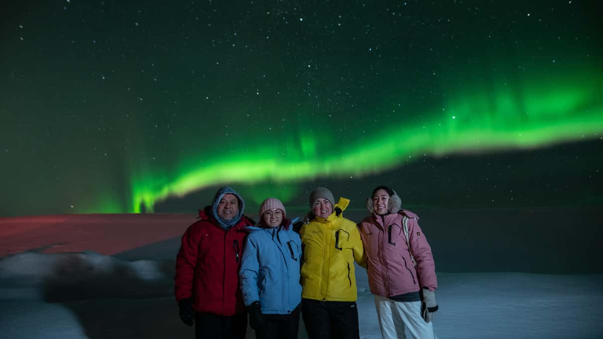 Gruppe in bunten Winterjacken beim Gruppenfoto unter grünem Polarlicht in Island