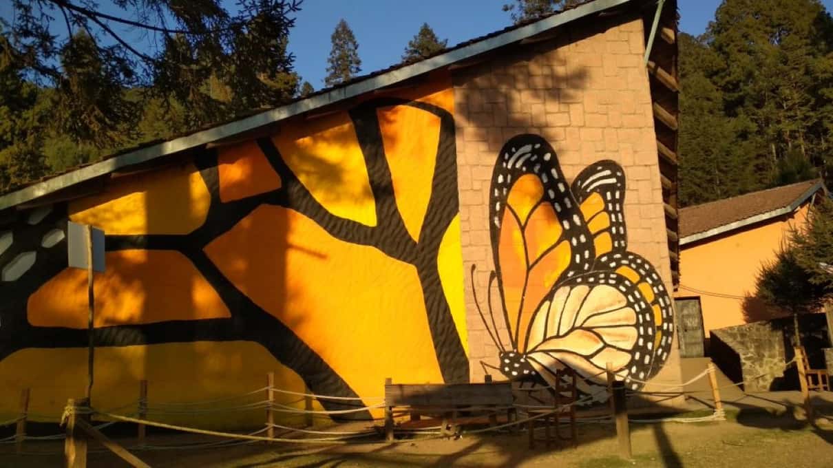 A wall painted with huge orange monarch wings beside a sanctuary building in the mountains of Michoacán