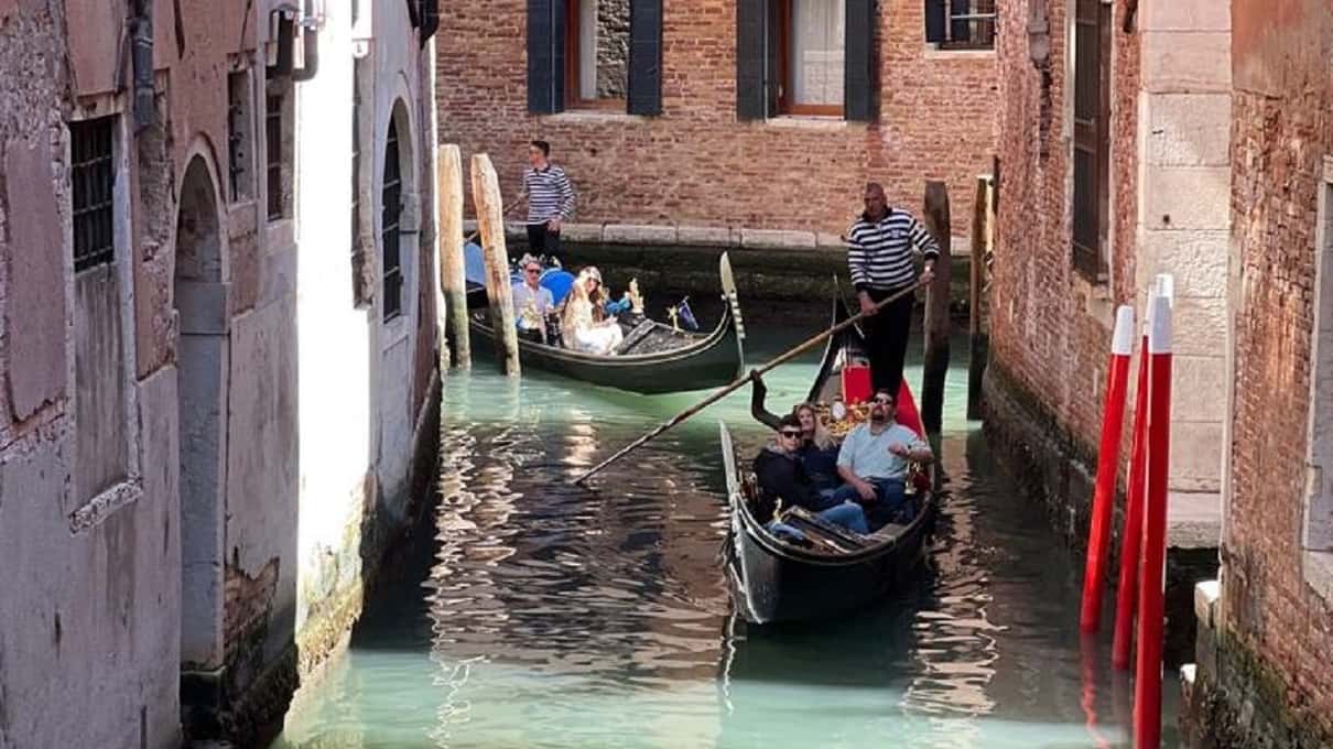 Twee gondels achter elkaar in een smal kanaal tussen oude gevels, voorop een gondelier in gestreept shirt