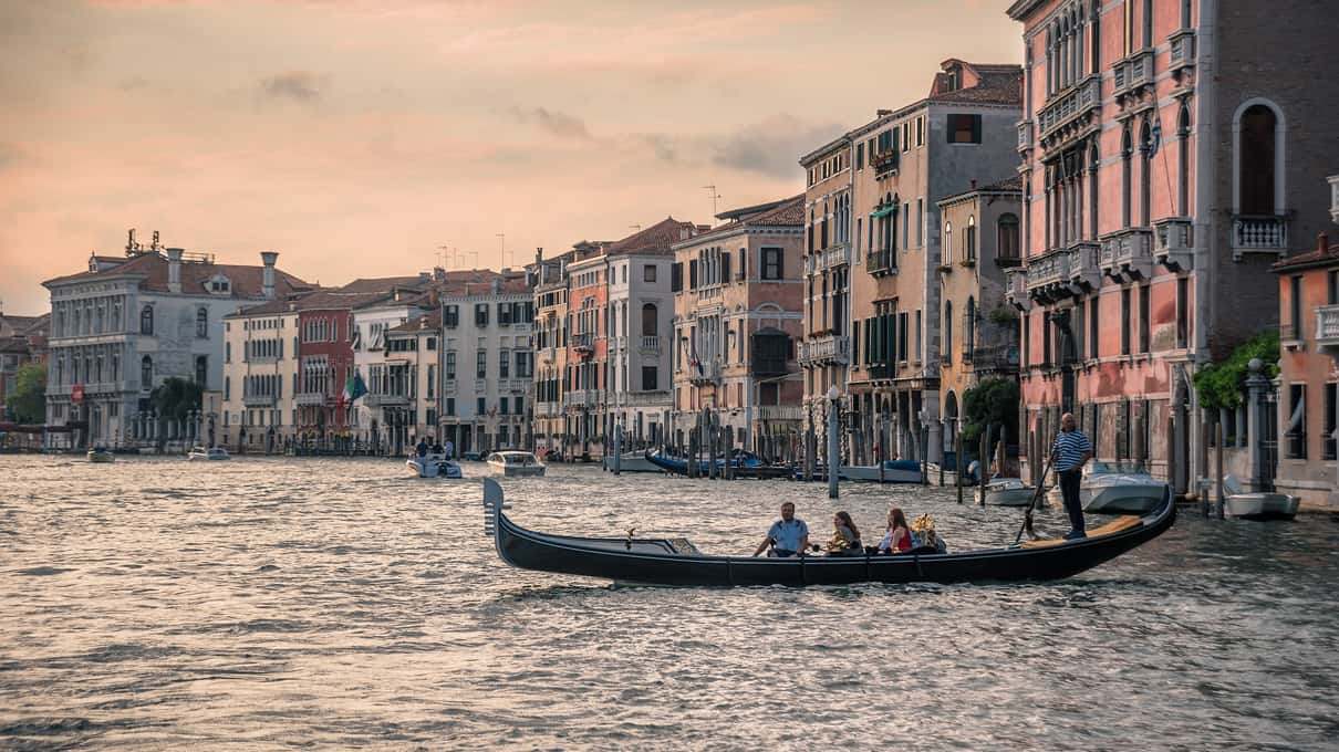 Gondola con passeggeri sul Canal Grande al tramonto, tra palazzi dalle facciate rosa e ocra