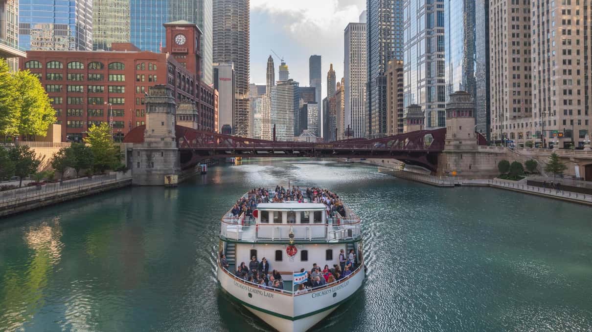 The Chicago's First Lady cruise boat with passengers on deck on the green river below skyscrapers