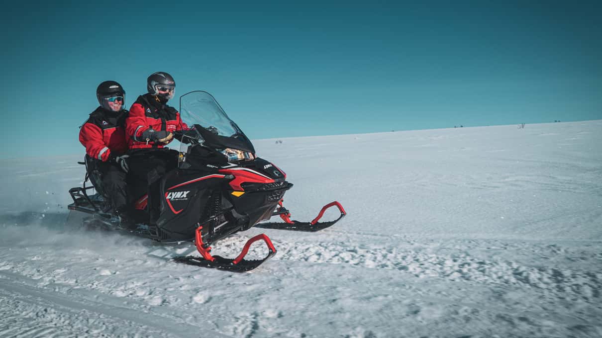 A rider in a red thermal suit alone on a snowmobile on bright snow during an Æventyr tour from Alta
