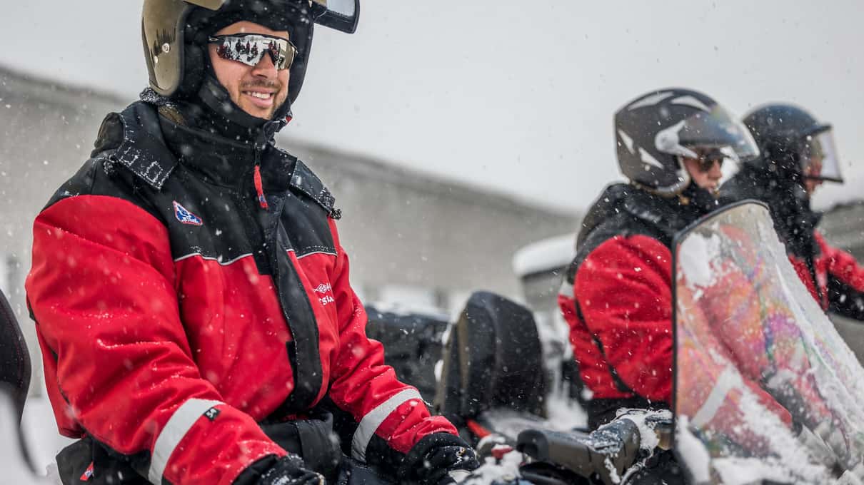 Close-up of snowmobile riders in red thermal suits and helmets on a winter tour above Alta