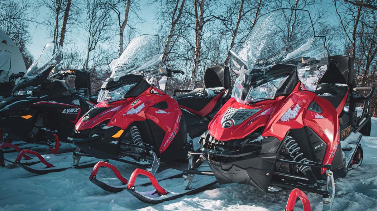 Two red snowmobiles parked side by side in bright snow on an Æventyr ride near Alta