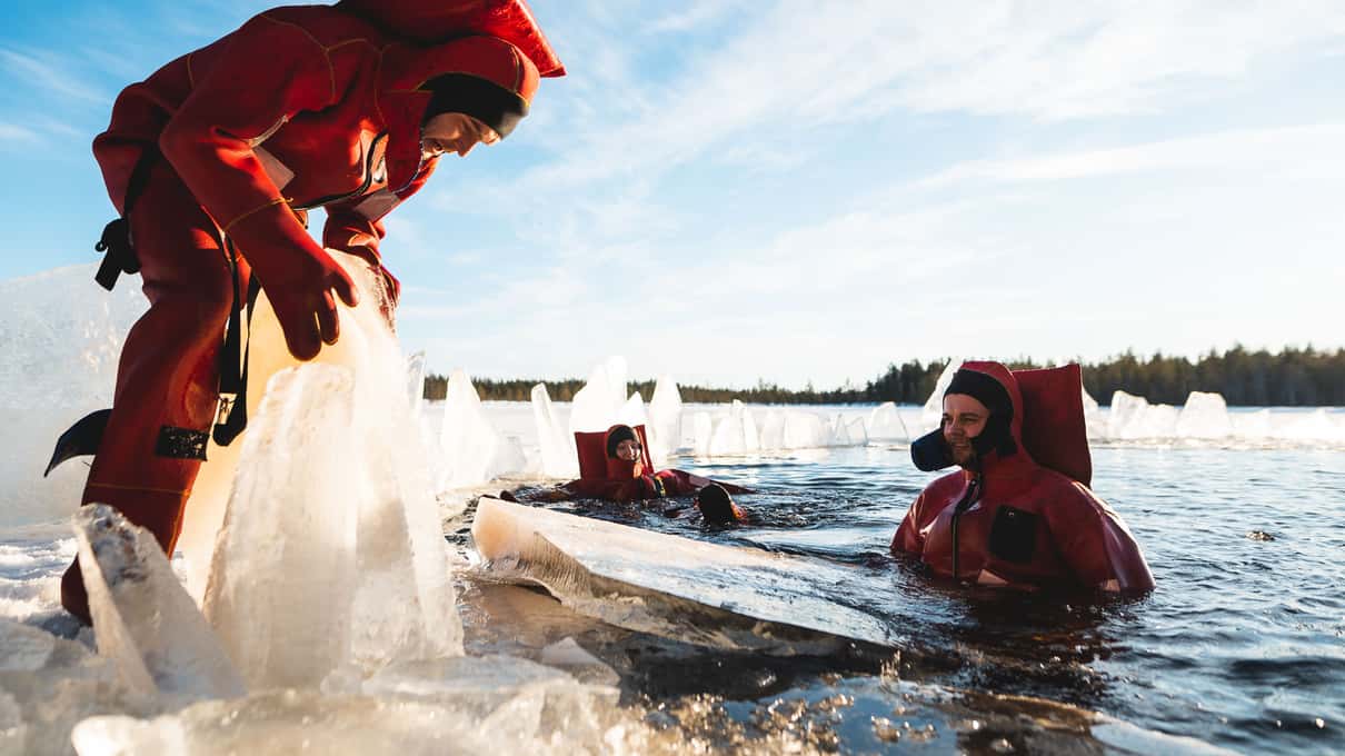 A floater in a red rescue suit sliding off the ice edge into the dark water of the lake