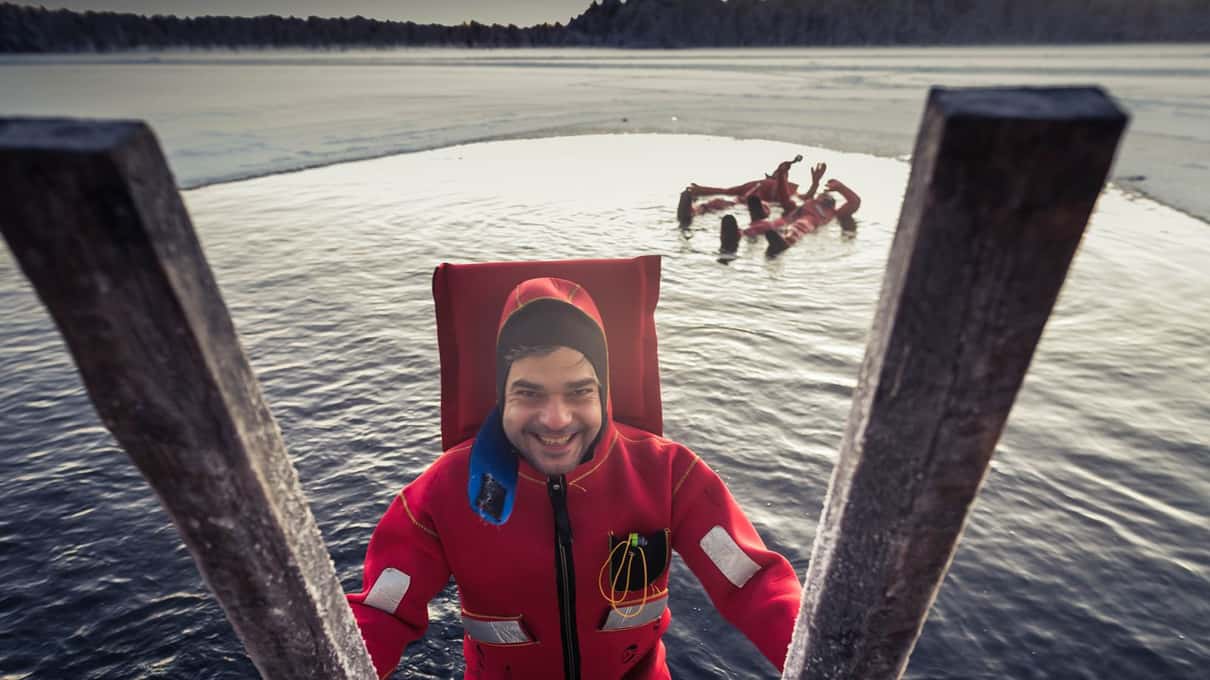 A smiling floater in a red rescue suit lying in the ice hole between the ladder rails