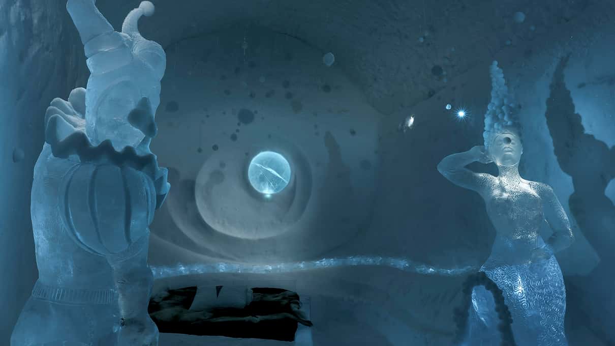 Two ice sculptures of human figures standing in a dim blue Icehotel art suite
