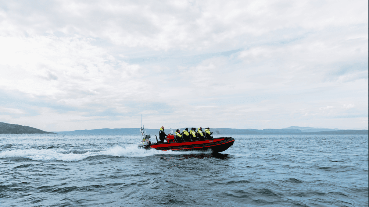 A red RIB boat full of guests in yellow floating suits speeding across the fjord near Kirkenes