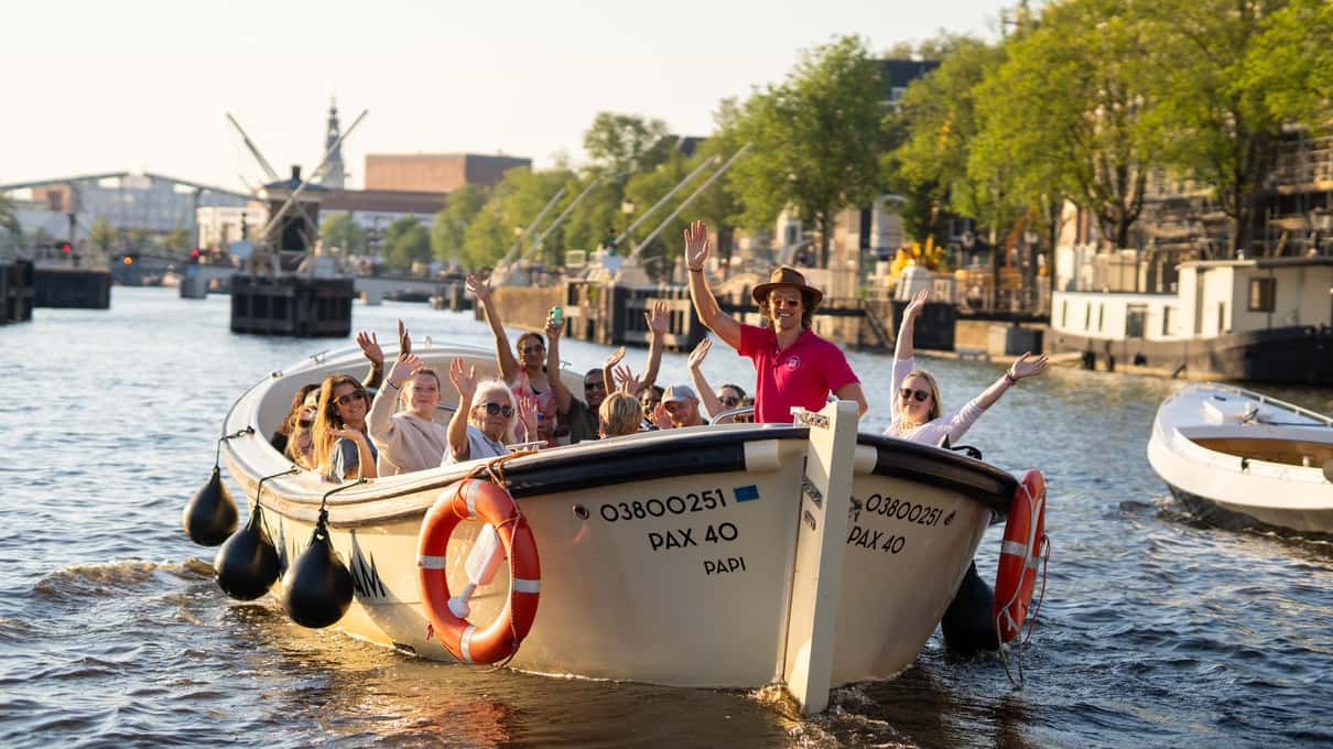 Otwarta biała łódź Captain Jack z machającymi pasażerami płynie szerokim kanałem w słoneczny dzień