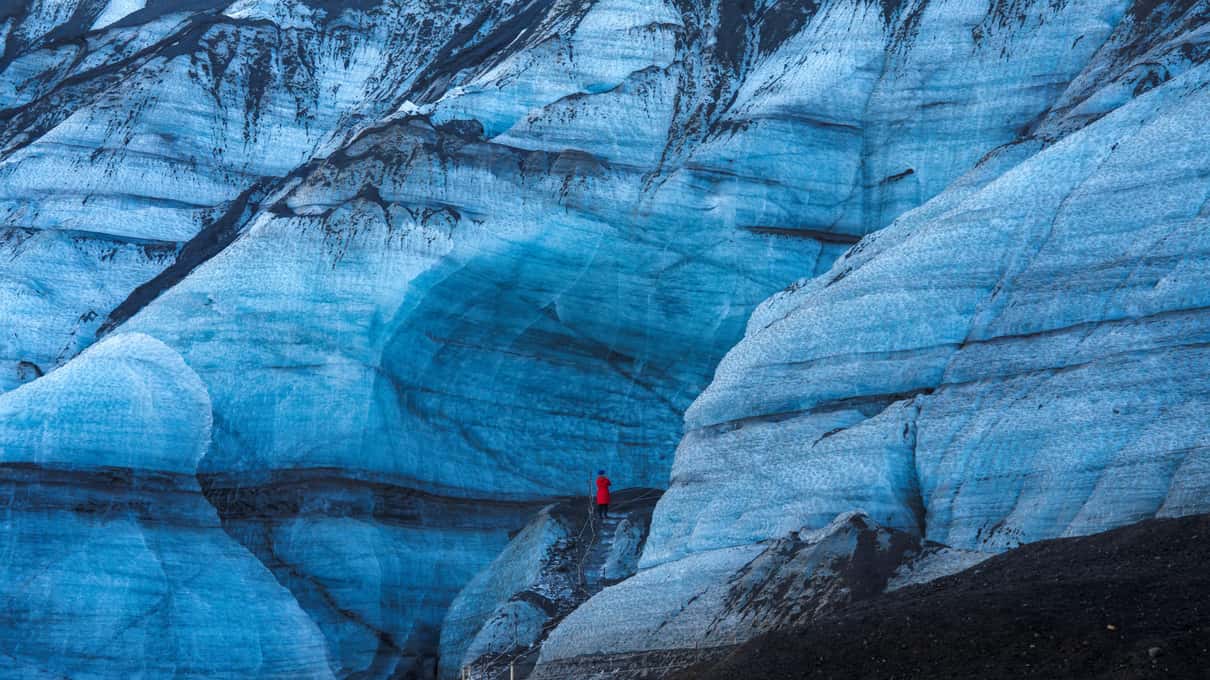 Blue glacier ice streaked with dark bands of volcanic ash on an Arctic Adventures tour