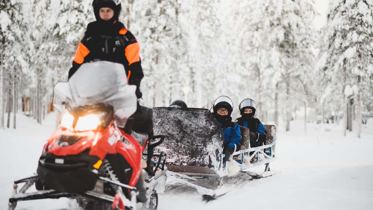 A guide's snowmobile pulling a covered sleigh with children through the snow near Levi