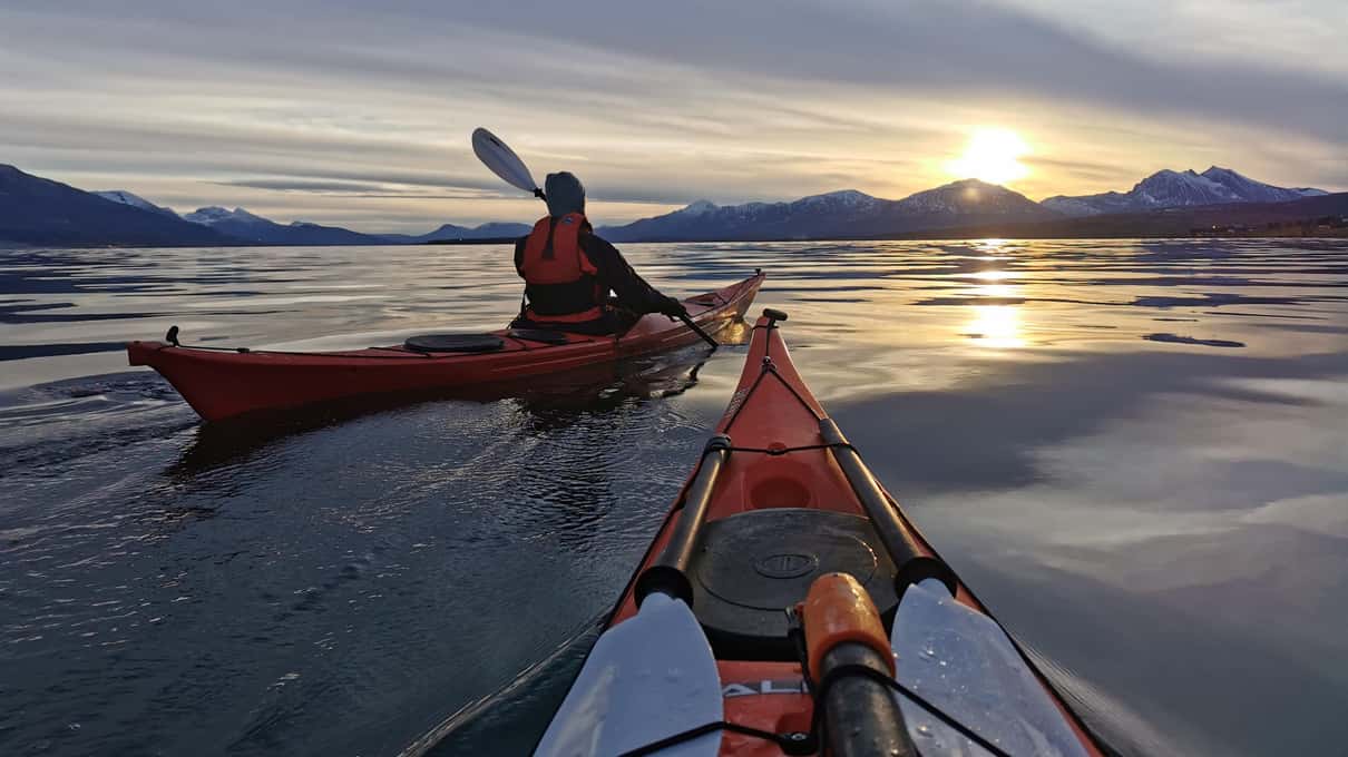 Two red sea kayaks on the fjord near Tromsø as the winter sun sits low on the mountains