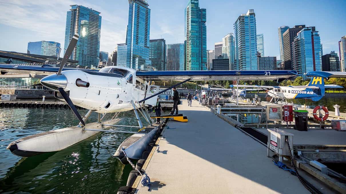 Harbour Air floatplane tied up at the Coal Harbour dock below the glass towers of downtown Vancouver